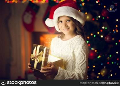 Closeup portrait of smiling girl in Santa cap posing with glowing gift box