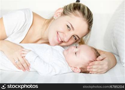 Closeup portrait of smiling mother lying with 3 months old baby on bed