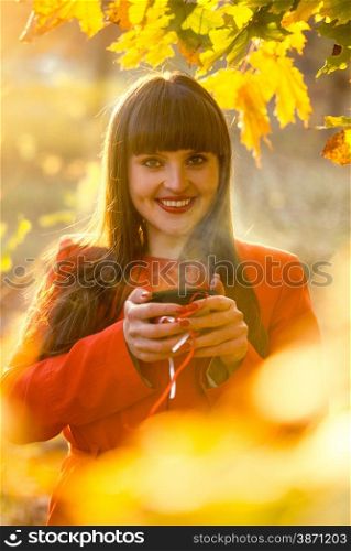 Closeup portrait of smiling woman holding hot of tea at autumn park