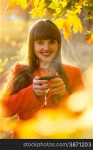 Closeup portrait of smiling woman holding hot of tea at autumn park