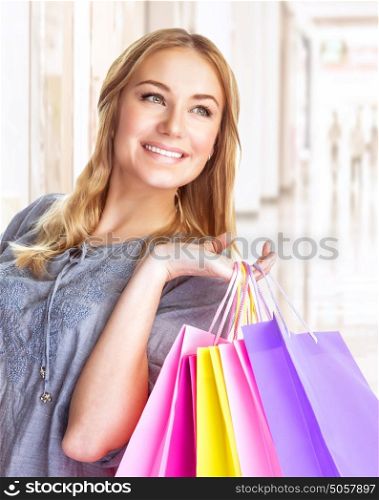 Closeup portrait of sweet cheerful girl standing in big shopping centre with colourful paper bags, doing purchase with pleasure