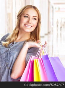 Closeup portrait of sweet cheerful girl standing in big shopping centre with colourful paper bags, doing purchase with pleasure