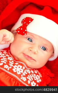 Closeup portrait of sweet little baby girl wearing red festive dress and Santa hat, having fun on Christmas party, wintertime holidays