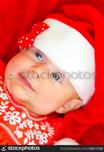 Closeup portrait of sweet little baby girl wearing red festive dress and Santa hat, having fun on Christmas party, wintertime holidays