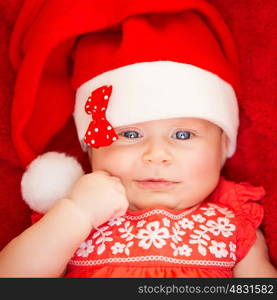 Closeup portrait of sweet little baby wearing Santa hat with stylish bow, red background, celebrating Christmas at home, joy and fun concept