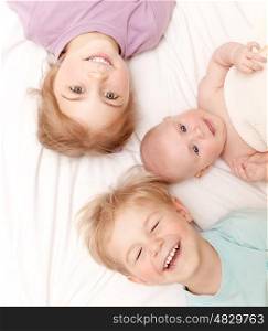 Closeup portrait of three cheerful kids lying down at home, newborn baby with brother and sister, happy family, love and friendship concept