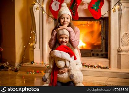 Closeup portrait of two beautiful girls in sweaters sitting at fireplace at house