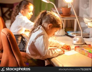 Closeup portrait of two little schoolgirl sitting behind table and drawing pictures
