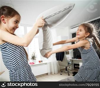 Closeup portrait of two little sisters fighting with pillows