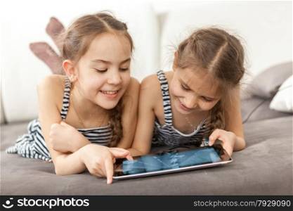 Closeup portrait of two smiling girls lying on couch and using tablet