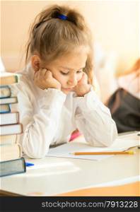 Closeup portrait of upset schoolgirl looking at textbook with homework
