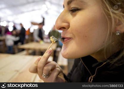 Closeup portrait of woman eating baked snail at outdoor cafe