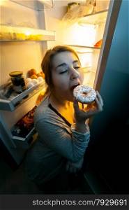 Closeup portrait of woman in pajamas eating donut on kitchen at night
