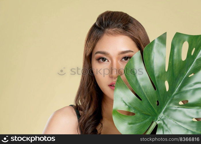 Closeup portrait of young ardent woman with healthy fair skin holding big green leaf near her face. Skin care beauty care concept.. Closeup young ardent woman with healthy skin holding green leaf near her face.