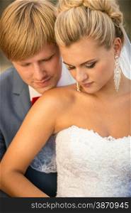 Closeup portrait of young handsome groom kissing blonde bride in shoulder