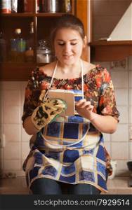 Closeup portrait of young housewife using tablet while cooking