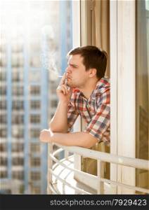 Closeup portrait of young man smoking cigarette out of window