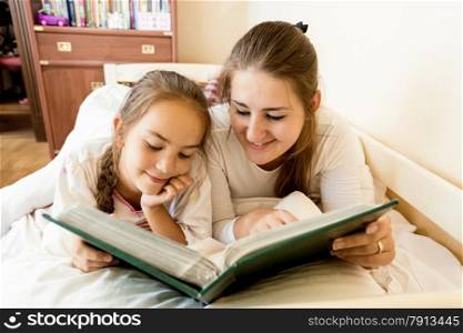 Closeup portrait of young mother and daughter lying in bed and viewing photo album