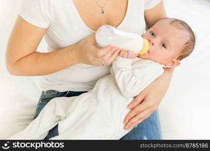 Closeup portrait of young mother holding her baby and feeding with milk from bottle