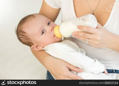 Closeup portrait of young mother holding her baby boy and feeding with milk