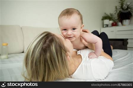 Closeup portrait of young smiling woman playing with baby on bed