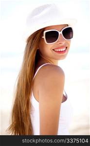 Closeup portrait of young smiling woman with white hat wearing sunglasses