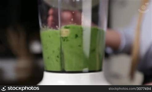Closeup process of blending avocado, broccoli, spinach, banana, parsley with blender to make healthy green smoothie. Woman preparing fresh raw green smoothie with blender. Healthy vegetarian diet for weight loss and detox