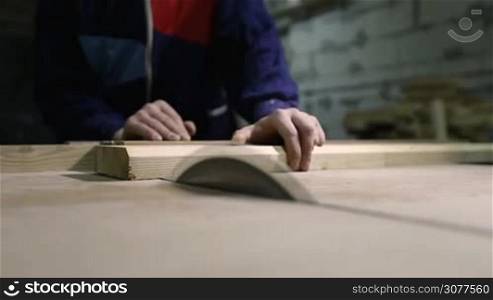 Closeup process of cutting wooden plank with table saw. Focus on circular saw blade. Carpenter sawing wooden board in workshop.