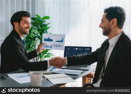 Closeup professional businessman shaking hands over desk in modern office after successfully analyzing pile of dashboard data paper as teamwork and integrity handshake in workplace concept. fervent. Closeup businessman handshake over desk with BI papers. fervent