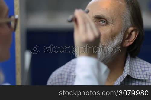 Closeup professional female doctor checking senior male patient&acute;s eyesight with flashlight in medical office. Young female neurologist holding flashlight while testing puppillary reflex of elderly man in clinic. Physician inspecting reflexes of man.