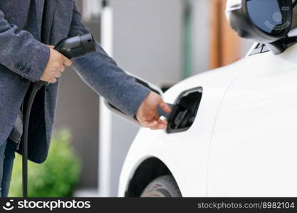 Closeup progressive asian man install cable plug to his electric car with home charging station. Concept of the use of electric vehicles in a progressive lifestyle contributes to clean environment.. Closeup progressive asian man recharge his EV car at home charging station.