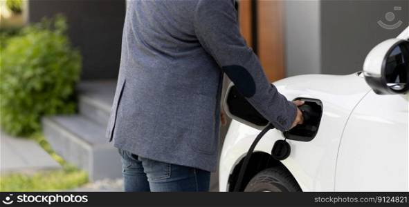 Closeup progressive asian man install cable plug to his electric car with home charging station. Concept of the use of electric vehicles in a progressive lifestyle contributes to clean environment.. Closeup progressive asian man recharge his EV car at home charging station.