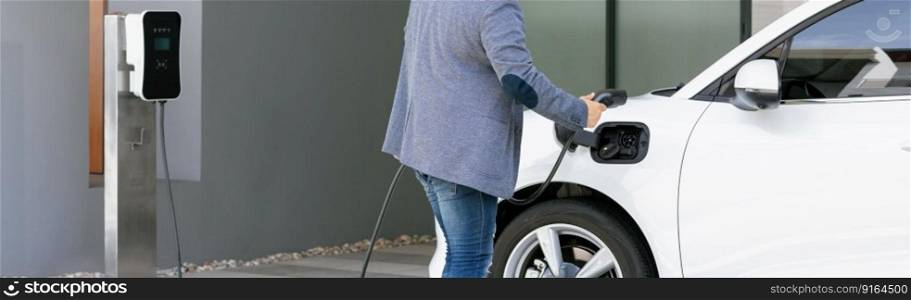 Closeup progressive asian man install cable plug to his electric car with home charging station. Concept of the use of electric vehicles in a progressive lifestyle contributes to clean environment.. Closeup progressive asian man recharge his EV car at home charging station.