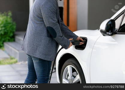 Closeup progressive asian man install cable plug to his electric car with home charging station. Concept of the use of electric vehicles in a progressive lifestyle contributes to clean environment.. Closeup progressive asian man recharge his EV car at home charging station.