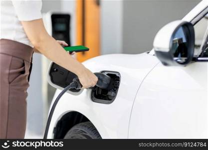 Closeup progressive woman install cable plug to her electric car with home charging station. Concept of the use of electric vehicles in a progressive lifestyle contributes to clean environment.. Closeup progressive woman recharge her EV car at home charging station.
