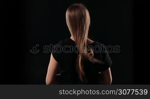 Closeup rear view shot of blond woman with straight long hair in a knot, letting it down isolated on black background. Back view of young female with wonderful fluttering straight hair in the wind. Slow motion.