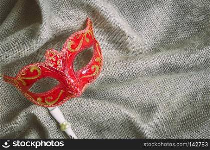 Closeup red carnival mask, Venetian mask  Opera mask  with white wood handle on the burlap sackcloth Fantasy concept, Photo booth props