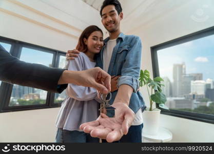 Closeup Sale representative hand offer the house key chain to Asian young couple after signed contact purchase or rental on the working space table in new place,Moving and House Hunting concept