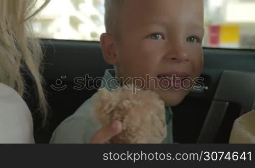 Closeup shot of a boy sitting on the back seat of the car and holding plush toy teddy bear in hands