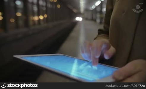 Closeup shot of a female hands holding tablet and writing letters in it. Tube train arrival is on the background.