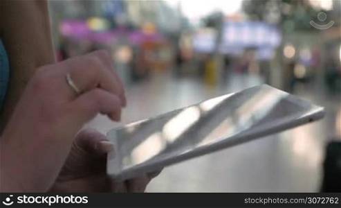 Closeup shot of a female hands holding tablet PC and typing on it. There is people traffic of a railway station or airport on the background.