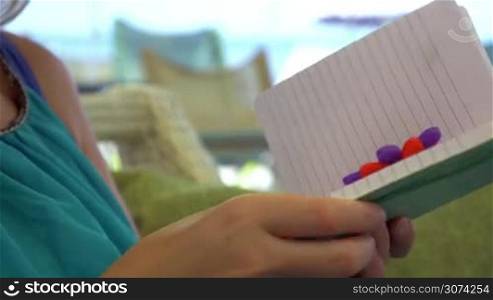 Closeup shot of a notebook in hands of young woman, she is writing in it with a pen with toy flower on the end.