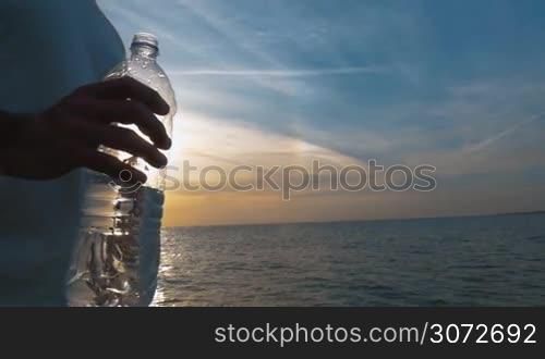 Closeup shot of a plastic water bottle in male hand. Setting sun is on the background.