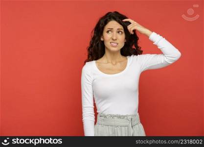 Closeup shot of curly millennial female minded thinking, creating solution planning idea looking up with hand on head and hair. Young woman pensive thinking isolated on red wall on copy space. Millennial female minded think on solution, plan or idea looking up isolated on red background