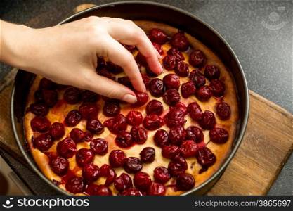 Closeup shot of female hand putting cherries on top of cheesecake
