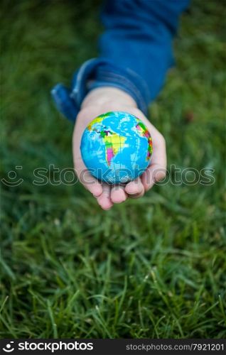 Closeup shot of girl holding small Earth globe in hand against grass background