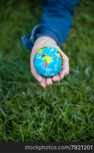 Closeup shot of girl holding small Earth globe in hand against grass background