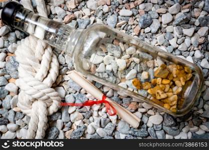 Closeup shot of letter, bottle and marine knot lying on pebbles
