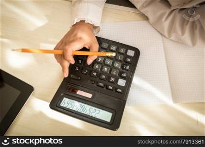 Closeup shot of little girl holding pencil and using calculator