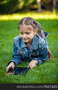 Closeup shot of little girl lying on grass with tablet